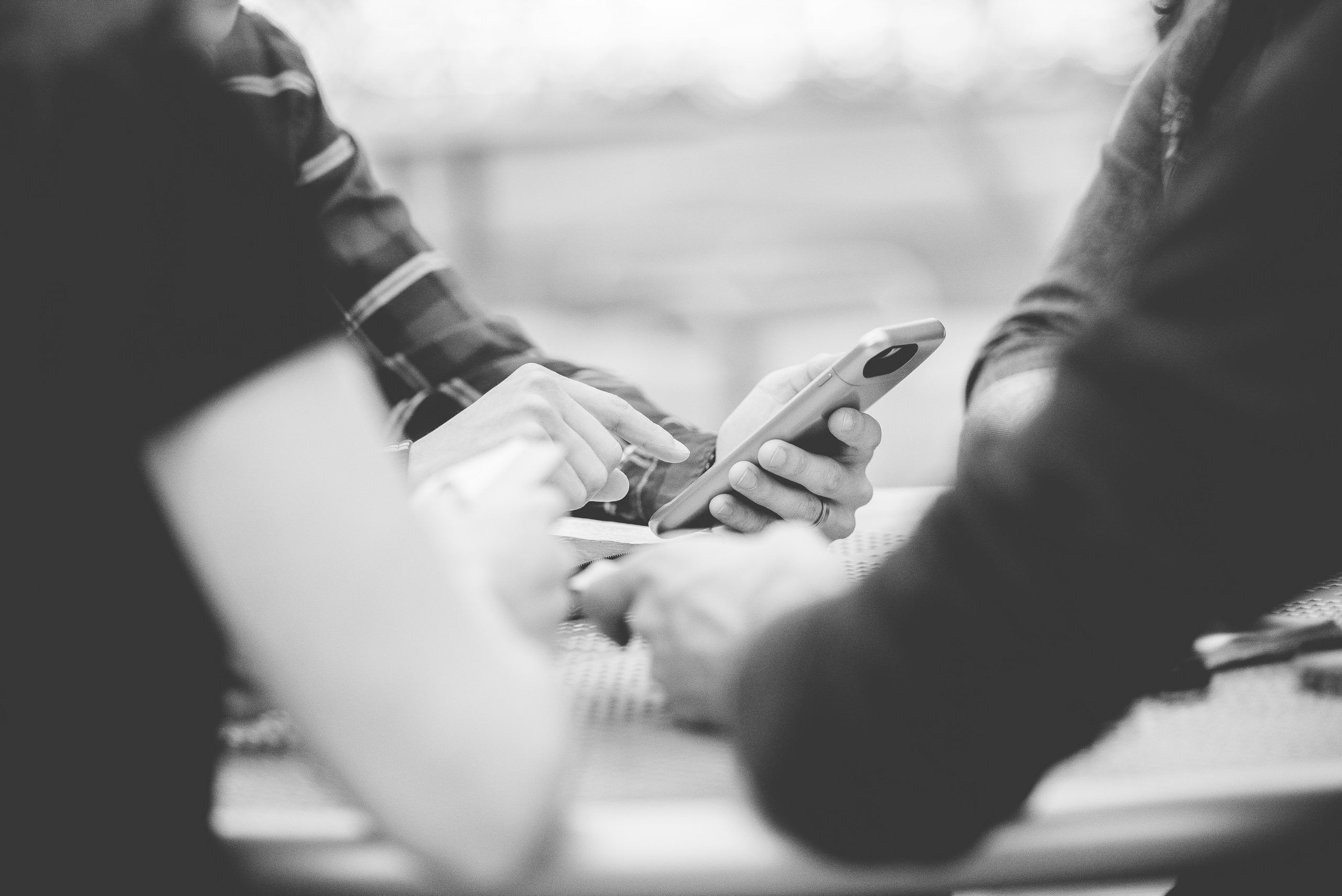 A closeup shot of people using their smartphone with a blurred background in black and white